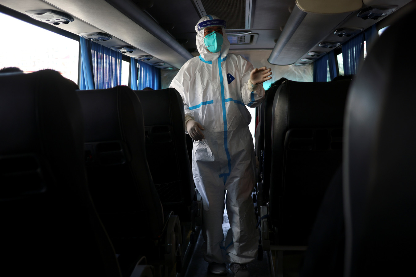 Een buschauffeur in beschermende kleding checkt reizigers voordat ze uit een  quarantainehotel 'ontslagen' worden in Dalian, China.