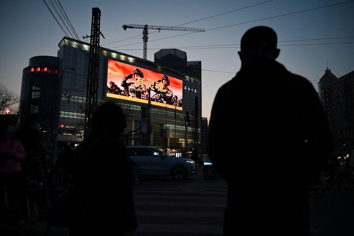 Mensen wachten bij een stoplicht in Peking en zien op de achtergrond een groot reclamebord met militaire propaganda.