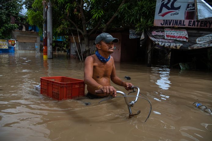 Een man waadt met zijn fiets door het water in zijn dorp in Kawit op de Filipijnen.