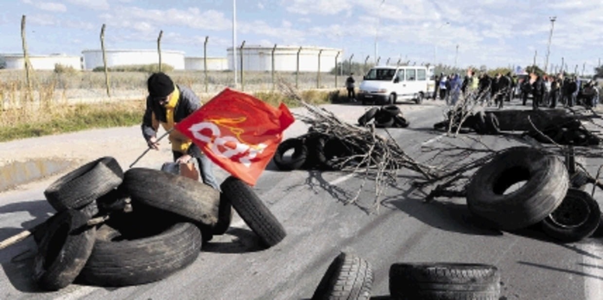 Een staker in Frontignan plant een vakbondsvlag in de barricade die een olie-opslagdepot blokkeert. (FOTO AFP ) Beeld AFP