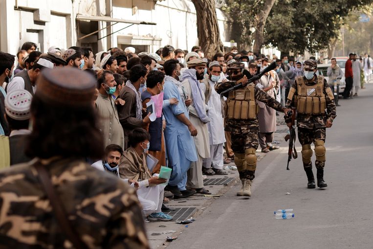 Talibansoldaten houden mensen in de gaten die bij de Iraanse ambassade in Kabul in de rij staan voor een visum.  Beeld REUTERS