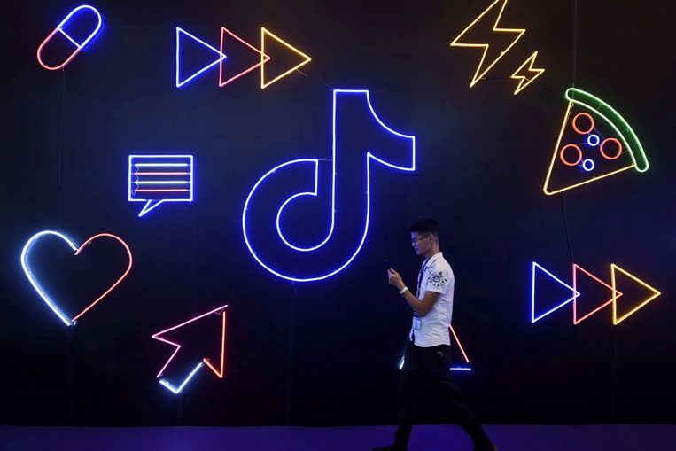 Een man loopt met zijn smartphone in de hand langs het logo van Tiktok. Beeld REUTERS