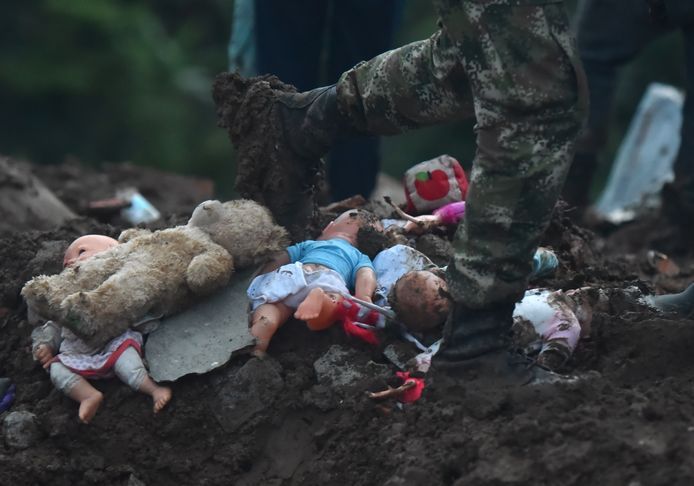 Een soldaat loopt langs speelgoed dat in de modder is achtergebleven na de landverschuiving.