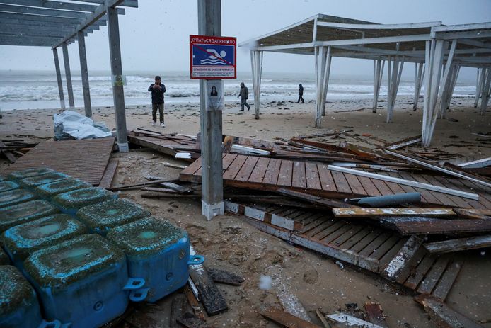 Des personnes marchent près de constructions endommagées sur une plage touchée par une puissante tempête à Yevpatoriya, en Crimée, le 27 novembre 2023.