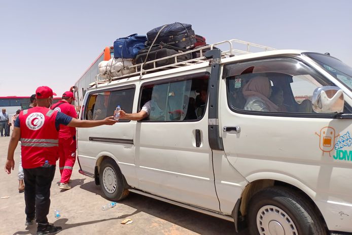 Een medewerker van de Rode Halve Maan geeft een flesje water aan Soedanese vluchtelingen in een busje aan de Egyptische kant van de grens met Soedan.