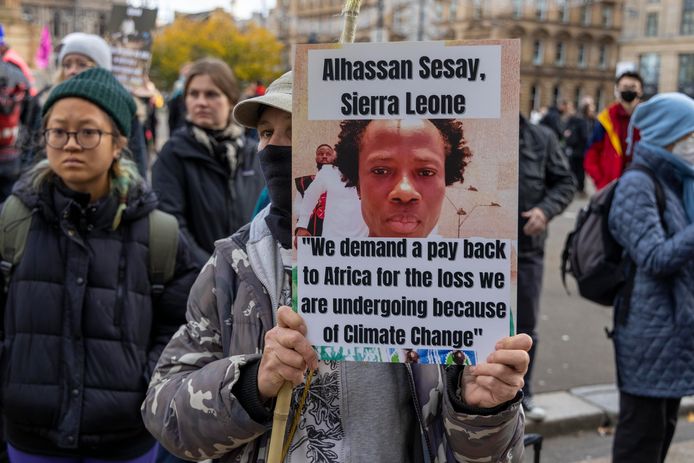 Een demonstrant houdt een bord omhoog met een uitspraak van een Afrikaanse klimaatactivist tijdens de COP26 in Glasgow. “We eisen een terugbetaling aan Afrika voor de verliezen die we vanwege klimaatverandering ondergaan", staat er op het bord geschreven.