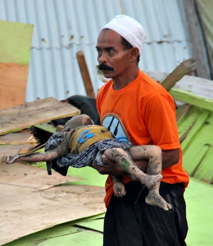 Een man draagt het lichaam van een kind in Palu.