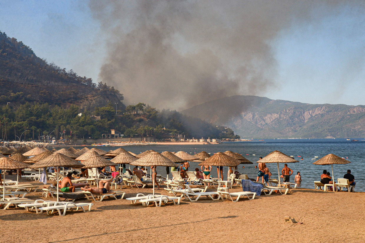 Toeristen in de omgeving van Marmaris houden vanaf het strand de ontwikkeling van de bosbranden in de gaten. Veel vakantiegangers zijn al vertrokken. Beeld AFP