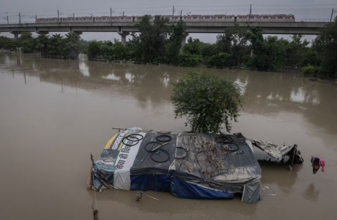 Metro rijdt op een brug terwijl huis wordt ondergedompeld in overstromingswater in New Delhi, India, 15 juli 2023.