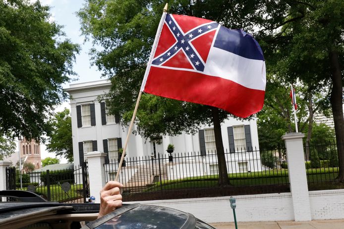 Een automobilist zwaait met een staatsvlag van Mississippi voor het huis van de gouverneur in Jackson tijdens een betoging om de vanwege de coronacrisis grotendeels stilgelegde economie in de staat weer te heropenen.