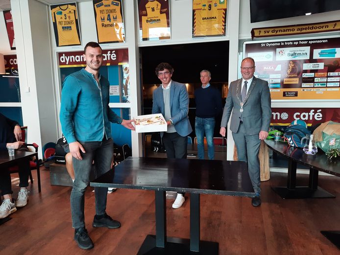 Dynamo-aanvoerder Freek de Weijer neemt een taart in ontvangst van sportwethouder Nathan Stukker en burgemeester Ton Heerts van de gemeente Apeldoorn. Op de achtergrond kijkt Draisma Dynamo-voorzitter Peter de Vries toe.