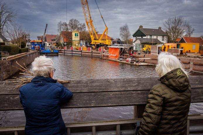 Twee dames staan op de brug belangstellend te kijken hoe het herstel van de kademuur in de kolksluis vordert.
