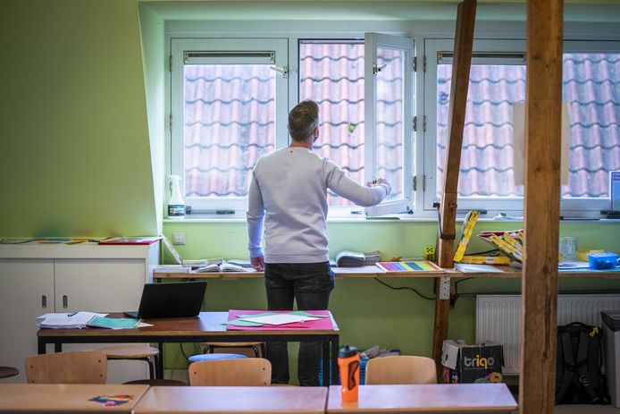 Een leerkracht opent een raam in een klaslokaal voor extra ventilatie.