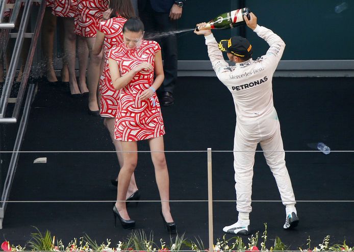 Lewis  Hamilton besprenkelt een grid girl met champagne na afloop van een GP.