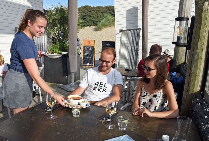 Gastvrouw Anouk serveert bij strandpaviljoen Ruig in Cadzand-Bad. Vooral in de horeca zijn 's zomers veel handen nodig. Dat heeft invloed op het aantal WW-uitkeringen in deze sector.