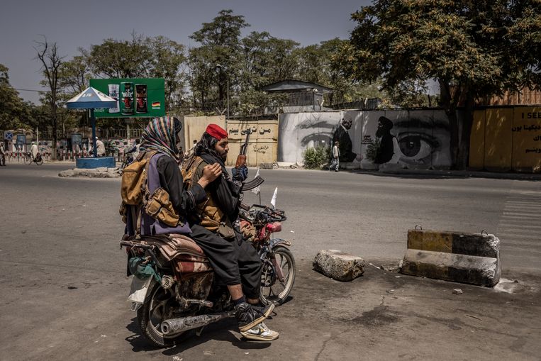 Talibanstrijders in Kaboel, met op de achtergrond een fresco dat het befaamde akkoord in Doha uitbeeldt, tussen Amerikaans gezant Zalmai Khalilzad en talibanleider Mullah Baradar. Dat akkoord was de directe aanleiding voor de Amerikaanse terugtrekking uit het land. Beeld Jim Huylebroek for The New York Times