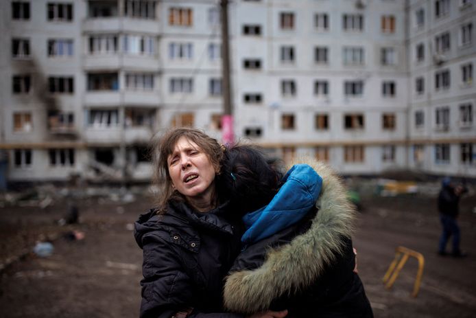 Een vrouw omhelst een andere vrouw voor een gebombardeerd appartementengebouw in Charkiv.