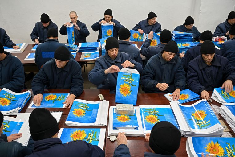 Gevangenen vouwen glanzende papieren vellen om tot een handtas. Op de omslagen staat een zonnebloem waaronder de tekst: ‘Geboorteland Oekraïne’, ook te vertalen als ‘Geliefd Oekraïne’. Beeld Stanislav Krupar