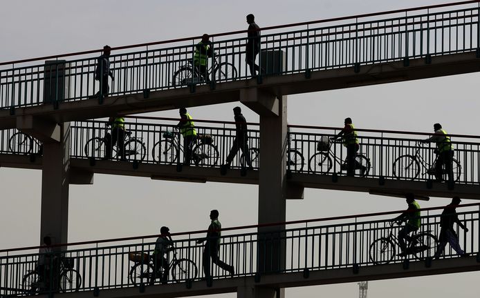 Aziatische arbeiders lopen over een voetgangersbrug in Dubai. Foto Karim Sahib