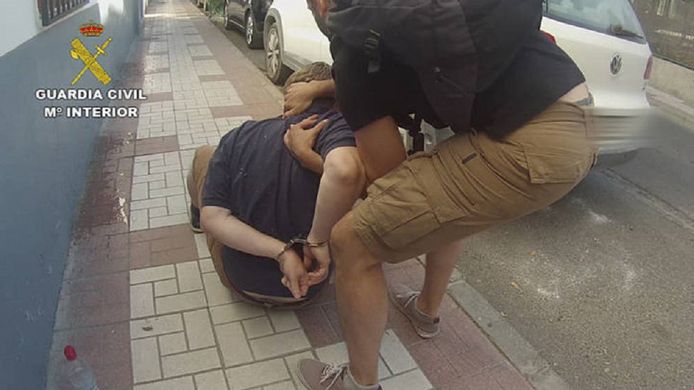 Een Spaanse politieman in burger heeft David Hayes in de boeien geslagen en neemt hem in een houdgreep.