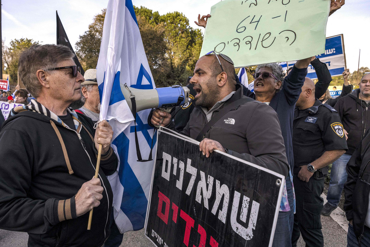 Een rechtse activist (rechts) tijdens een linkse demonstratie tegen de coalitie die Netanyahu probeert te vormen. Op het bord staat 'Linksen zijn verraders' in het Hebreeuws.  Beeld Menahem Kahana / AFP