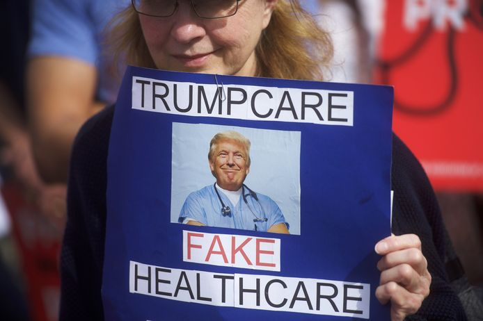 Een betoger houdt  een bord vast met: 'Trumpgezondheidszorg, neppe gezondheidszorg' tijdens een demonstratie