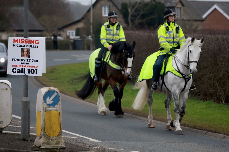 Politiemannen te paard rijden langs een bord waarop aandacht wordt gevraagd voor de verdwenen Nicola Bulley.  Beeld REUTERS