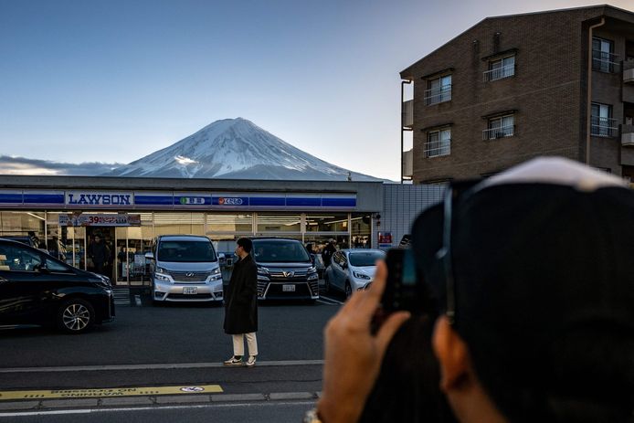 Een toerist poseert voor een supermarkt, met Mount Fuji op de achtergrond. Het is een populaire plek voor foto's.