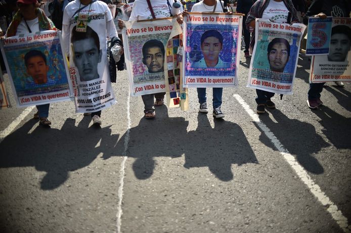 De ouders van de vermoorde studenten houden hun foto’s  omhoog terwijl ze opstappen in Mexico-Stad.