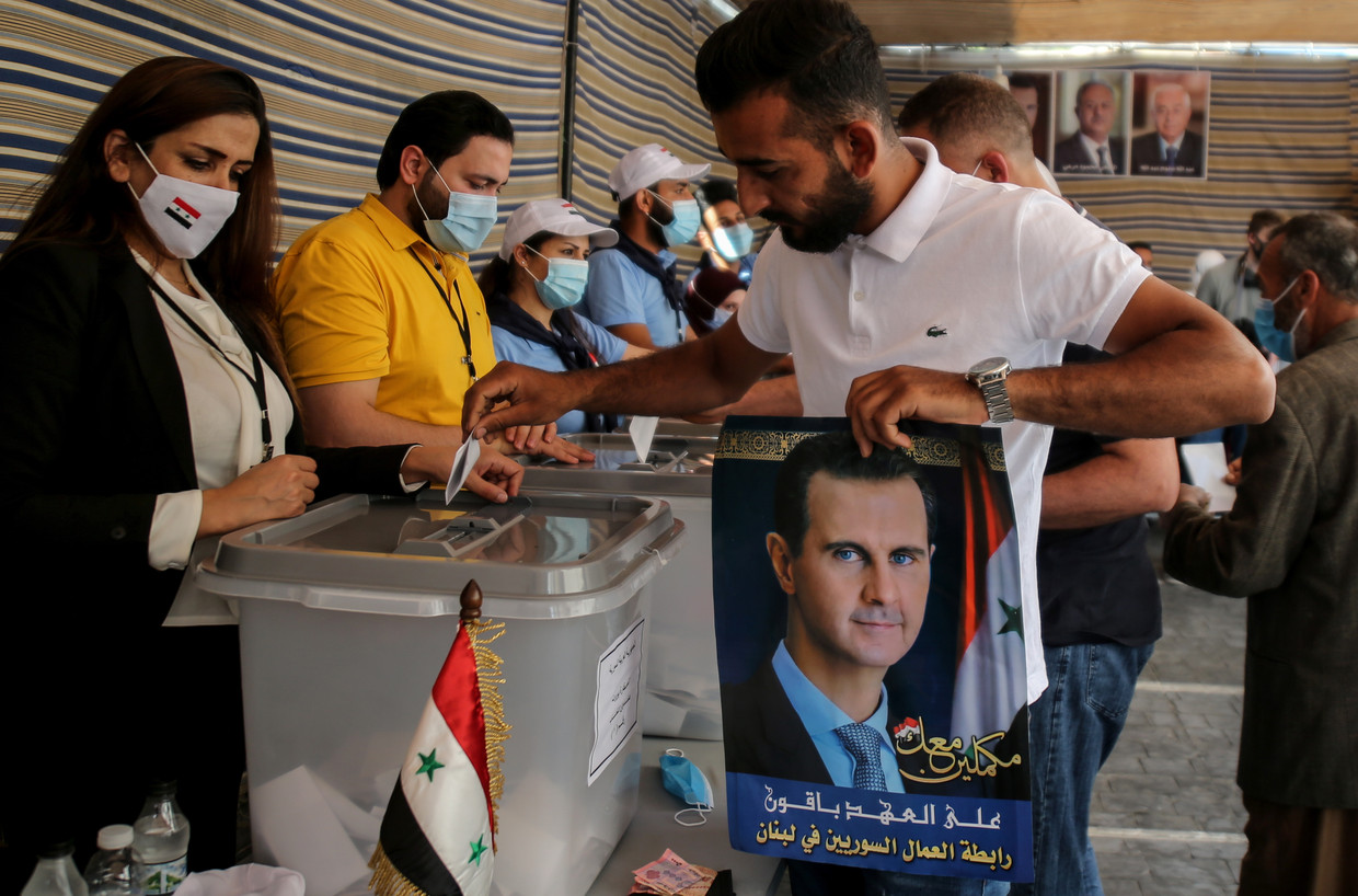 Een stembureau in het Libanese Beiroet. Een Syrische vluchteling brengt zijn stem uit, in zijn handen een steunbetuiging aan president Assad. 'Die posters zijn alleen voor de show. Als je in het stemhokje staat, kun je stemmen op wie je wilt.' Beeld EPA