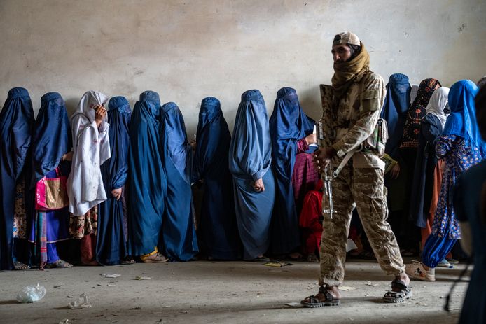 Een talibanstrijder in Kaboel houdt de wacht terwijl gesluierde vrouwen achter hem in de rij staan voor voedselhulp. Beeld van 23 mei 2023.