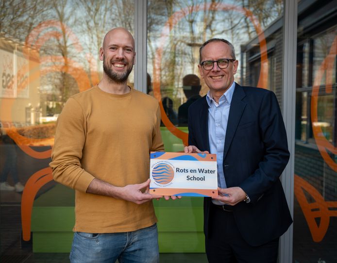 Directeur Adriaan Veenenbos (rechts) toont het nieuwe predicaat. De Rots & Water-training leert leerlingen soms hard te zijn als een rots en soms zacht als water, met als doel dat ze sterker in hun schoenen komen te staan.