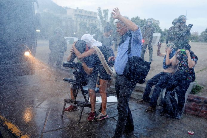 Mensen beschermen zich tegen een waterkanon dat de politie heeft ingezet.