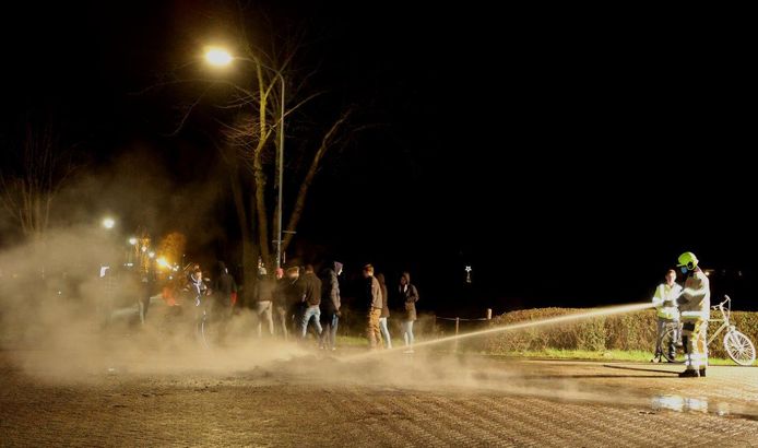 Groepjes jongeren kijken toe hoe de brandweer het vuur blust