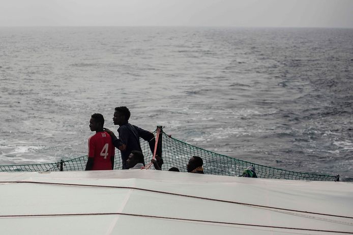 Migranten kijken naar de zee vanaf het dek van de ngo Proactiva Open Arms. In de Middellandse Zee zijn zondag 63 migranten vermist nadat hun rubberboot is gezonken voor de kust van Libië. Dat zegt de kustwacht van het Noord-Afrikaanse land.