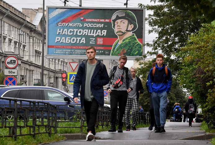 Jongemannen voor een billboard dat werken bij het leger promoot in Sint Petersburg. De slogan op de affiche: "Rusland dienen is een echte job."