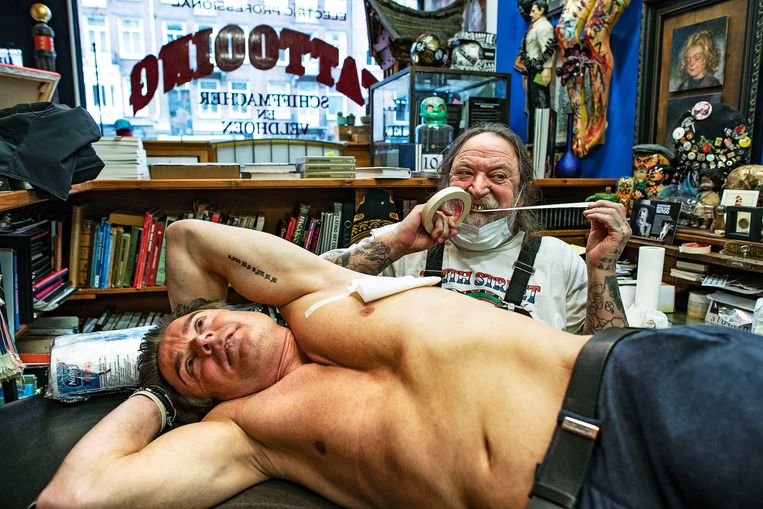 Henk Schiffmacher heeft net een tattoo gezet op de rug van een klant en doet er een gaasje op. Beeld Guus Dubbelman / de Volkskrant