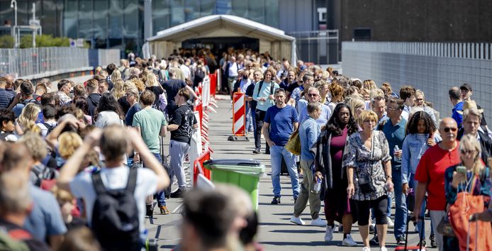 Reizigers tijdens het wachten in lange rijen buiten op Schiphol tijdens het pinksterweekend.