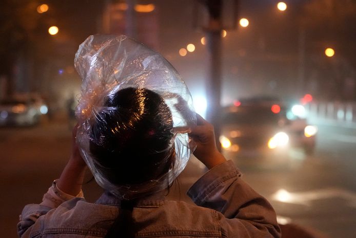 Een vrouw bedekt haar hoofd met een plastic zak tijdens de zandstorm in Peking.