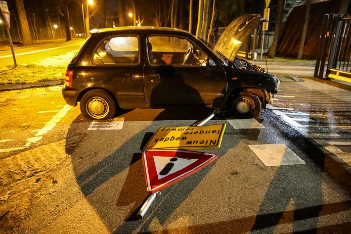 Het waarschuwingsbord zit vast onder de auto. Voor en achterband zijn lek gereden.