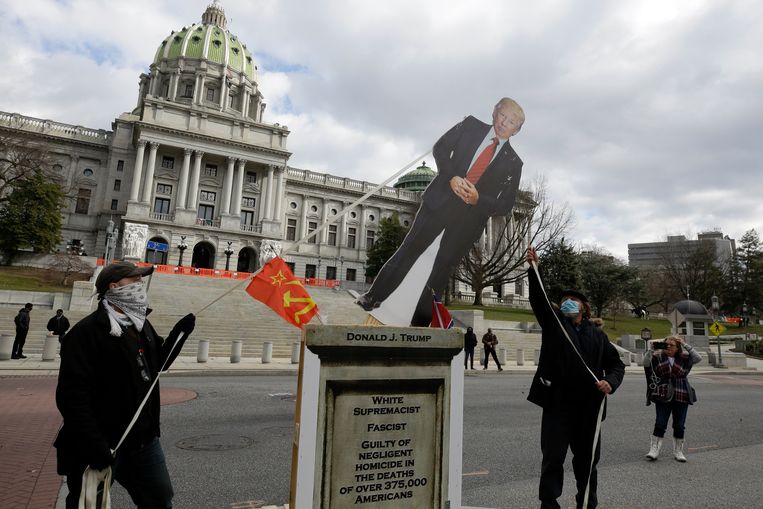 Activisten trekken een kartonnen 'standbeeld' van president Trump omver  voor het State Capitol van Pennsylvania in Harrisburg. Beeld AP