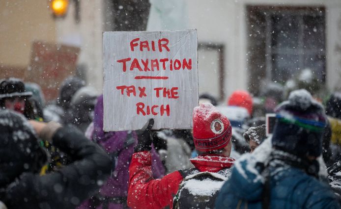 Demonstranten in Davos voor aanvang van het  World Economic Forum (WEF) dat vandaag begint. Op het bord staat de tekst 'eerlijke belastingen' en 'belast de rijken'.