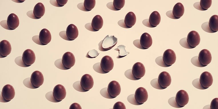 chocolate eggs placed in a pattern where one has cracked on a colored background Beeld Getty Images