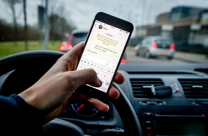 Een bestuurder verstuurt een bericht met zijn mobiele telefoon tijdens het rijden in de auto.