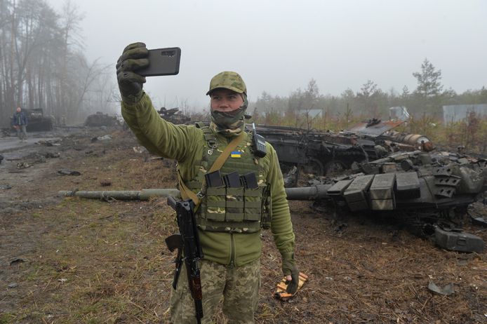 Een Oekraïense soldaat neemt een selfie voor een vernielde Russische tank