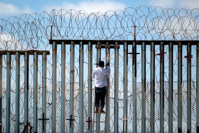 Een uigezette Mexicaanse migrant plaatst een houten kruis op een grenshek ter nagedachtenis aan alle migranten die gestorven zijn terwijl ze de VS probeerden te bereiken. Archiefbeeld van juli 2022.