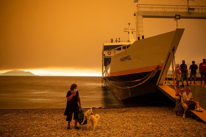 Een vrouw staat met haar hond bij de ferry. Op Evia woeden bosbranden.