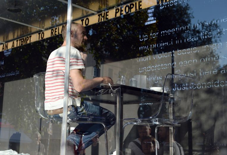 Kunstenaar Dries Verhoeven zit in een glazen container op het Heinrichplatz in Berlijn. Op de muur worden zijn teksten geprojecteerd. Beeld epa