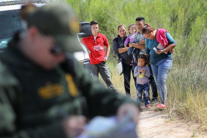 Een Centraal-Amerikaanse familie wacht aan de Amerikaanse kant van de grens terwijl een agent iets opschrijft.