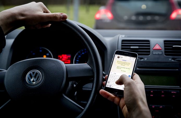 Een bestuurder verstuurt een bericht met zijn mobiele telefoon tijdens het rijden.